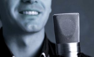 A condenser microphone with a voice actor smiling in the background.