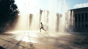 A boy runs through a splash pad with water spraying up from the ground.
