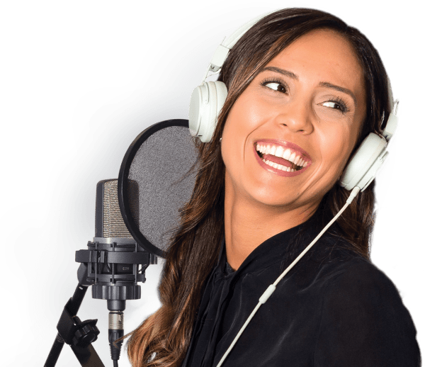 A voice actress smiling while wearing headphones and standing behind a microphone.