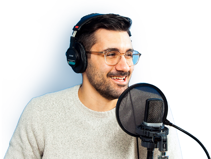 A voice actor smiling while wearing headphones and standing behind a microphone.