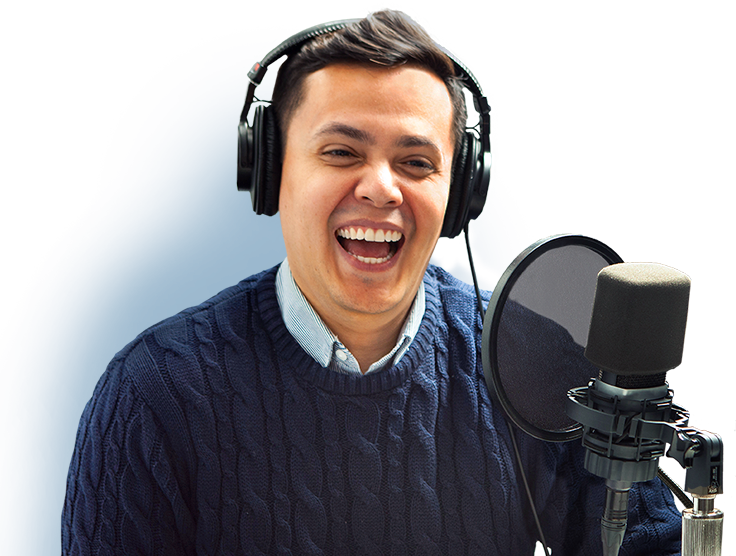 A voice actor laughing while wearing headphones and standing behind a microphone.