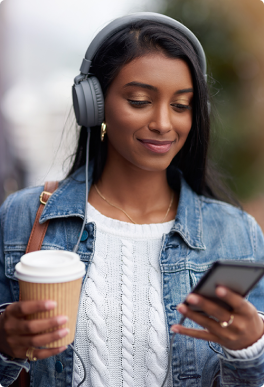 A woman holds a coffee while listening to audio on her phone